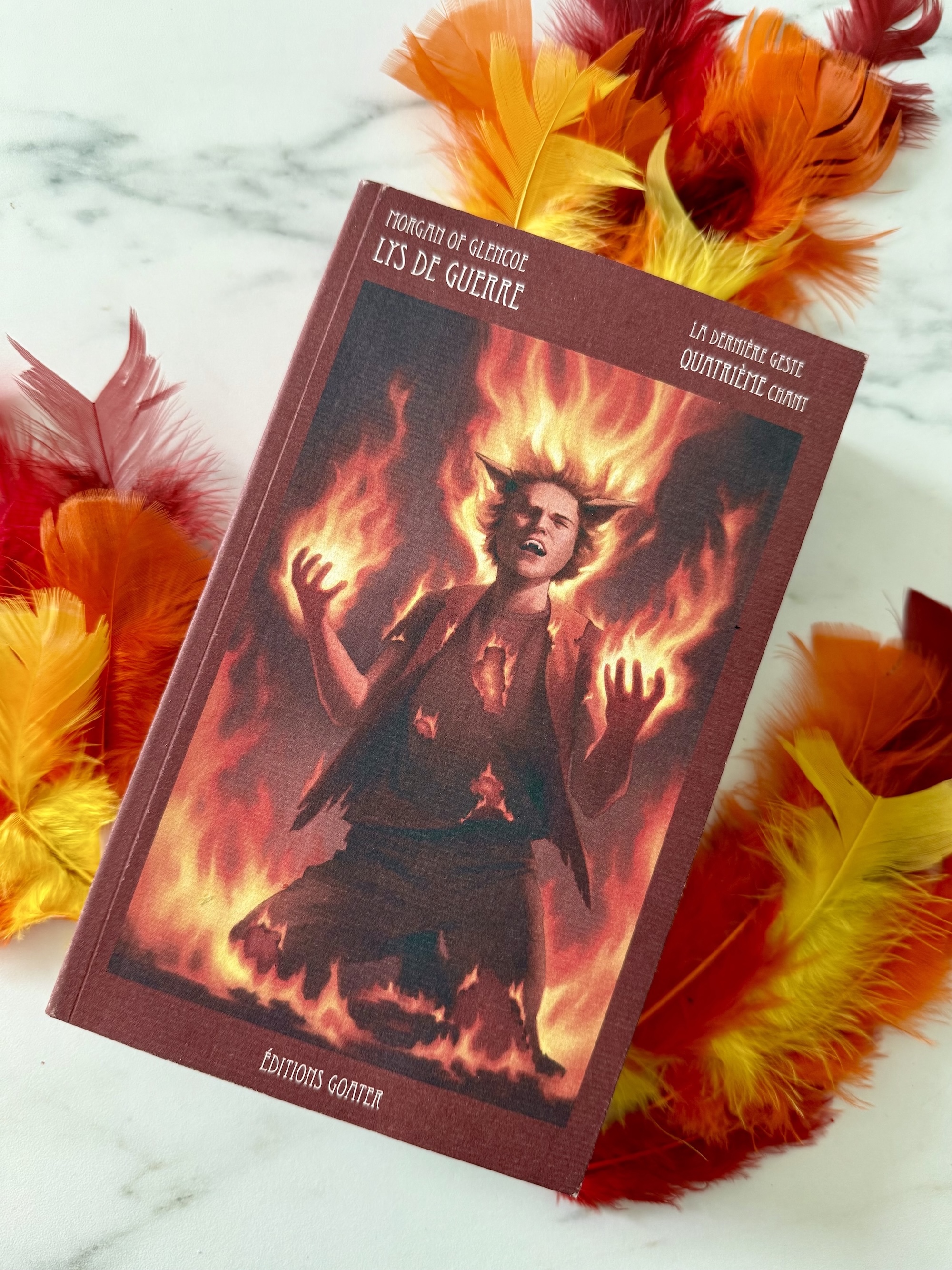 Livre posé avec autour des plumes jaunes, oranges et rouges symbolisant les flammes. La couverture de Lys de Guerre montre un personnage (Pyro) en flammes, hurlant, les genoux au sol. 