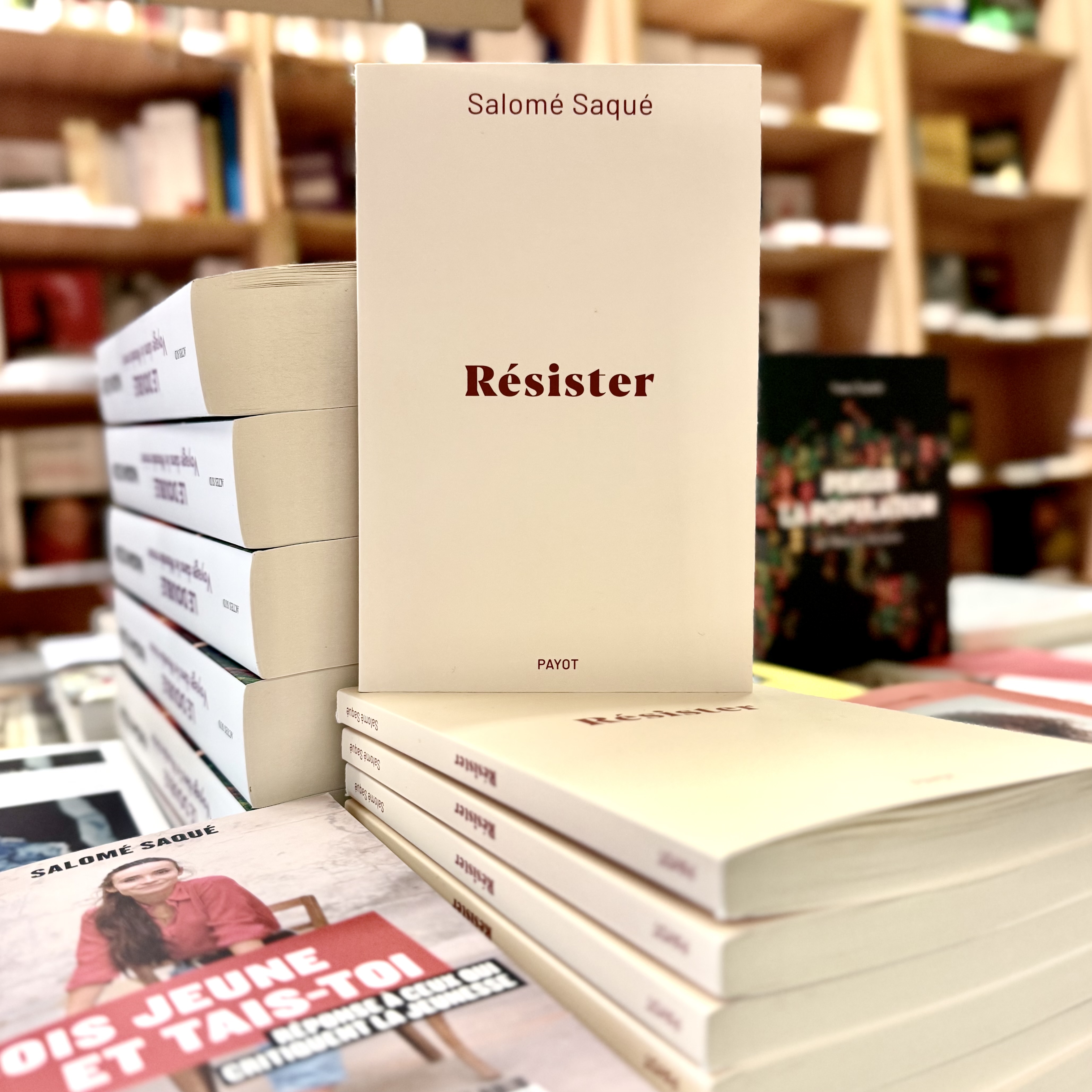 Pile de livre sur table en librairie avec un exemplaire de Résister en facing. La couverture de Résister est un fond beige sobre avec le titre écrit en rouge foncé dessus.